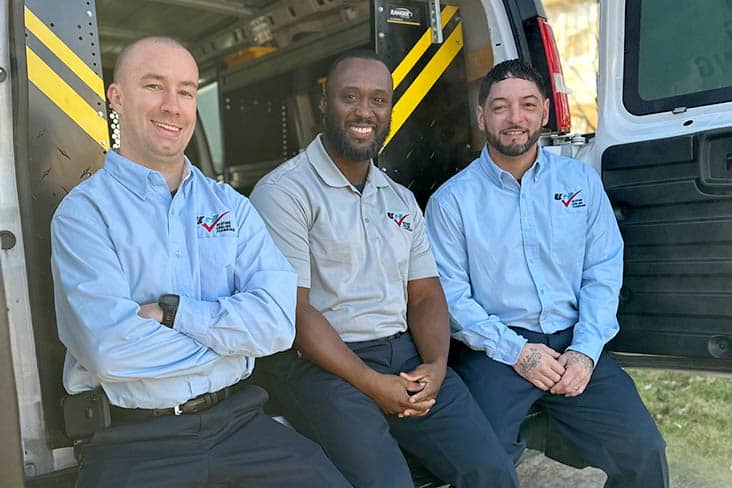 Three technicians sitting in the back of a work van smiling