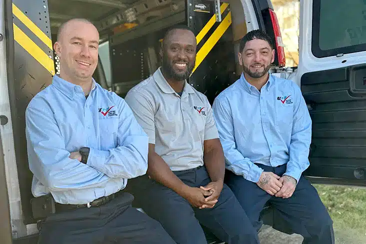 3 technicians sitting in the back of a van smiling