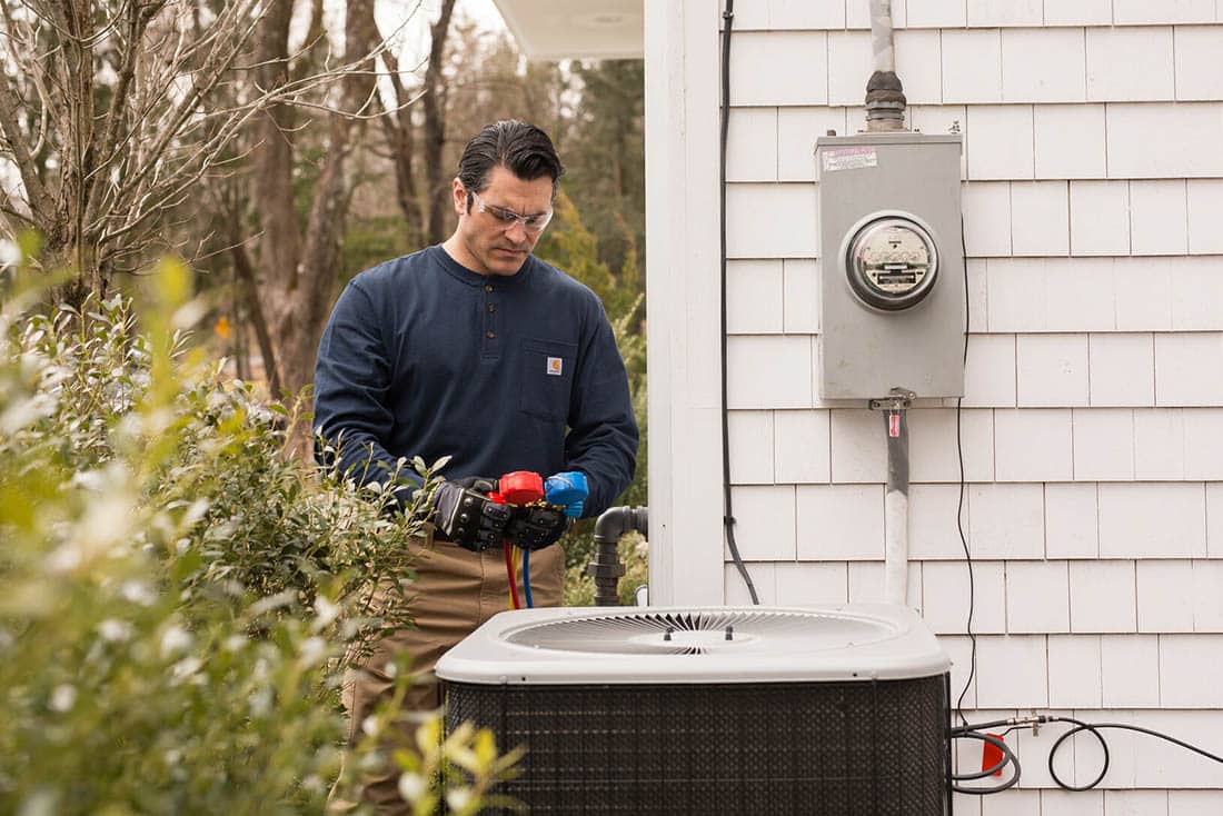 Technician performing air conditioner repair on an outdoor unit on side of house