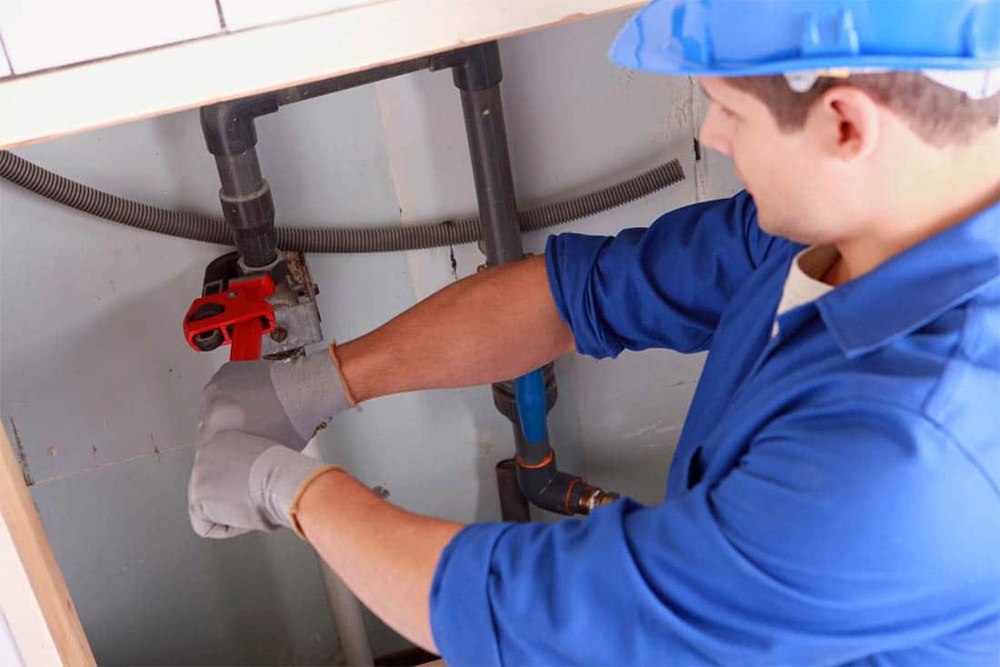 Plumber using a wrench to fix a leaky pipe under a sink