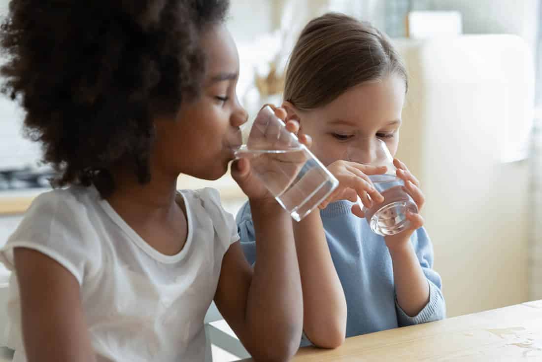 Two girls sitting in kitchen drinking purified water